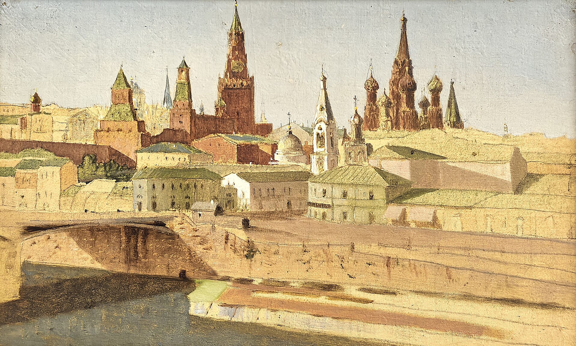 A sunlit view of the Moscow Kremlin from across the Moskva: the Spasskaya Tower, Kremlin wall towers and the onion domes of St Basil's Cathedral rise above pale houses, with the old Moskvoretsky Bridge and the riverbank below.