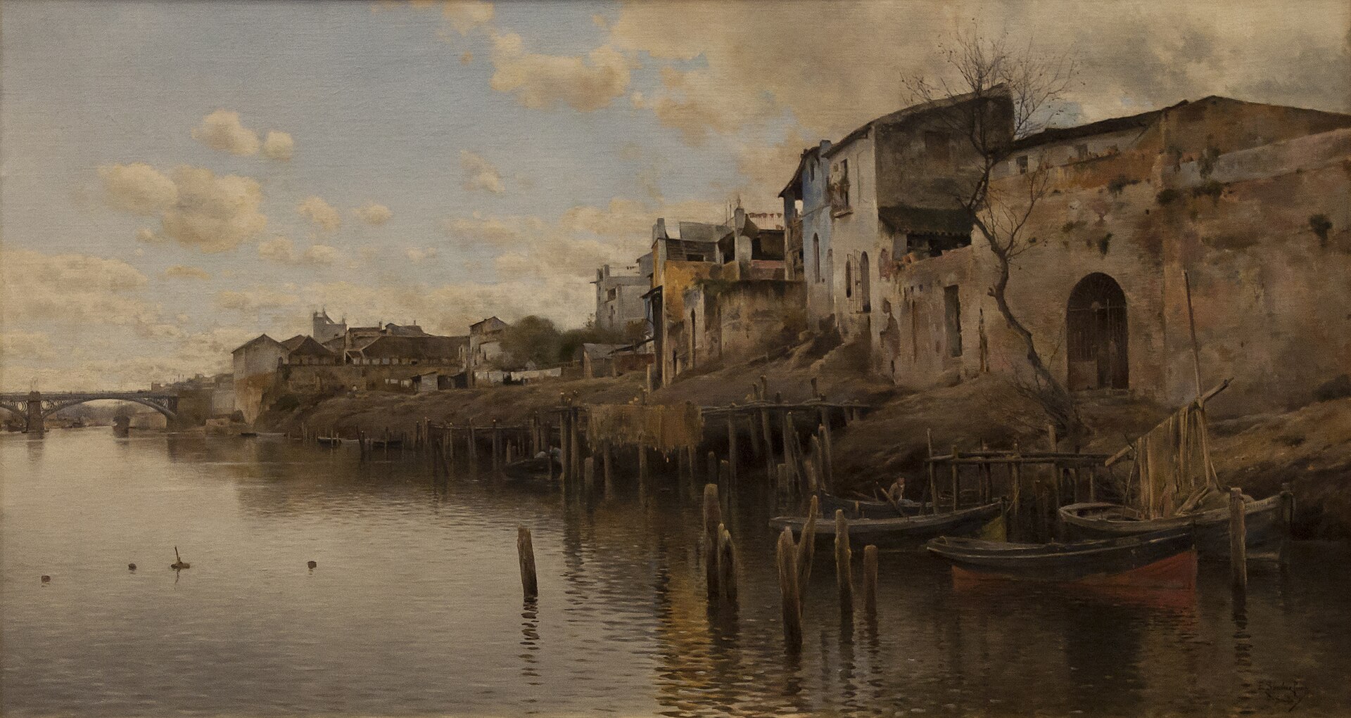 The Guadalquivir at Seville's Triana district: weathered riverside houses, wooden jetties and moored boats, with the iron Triana Bridge in the distance.