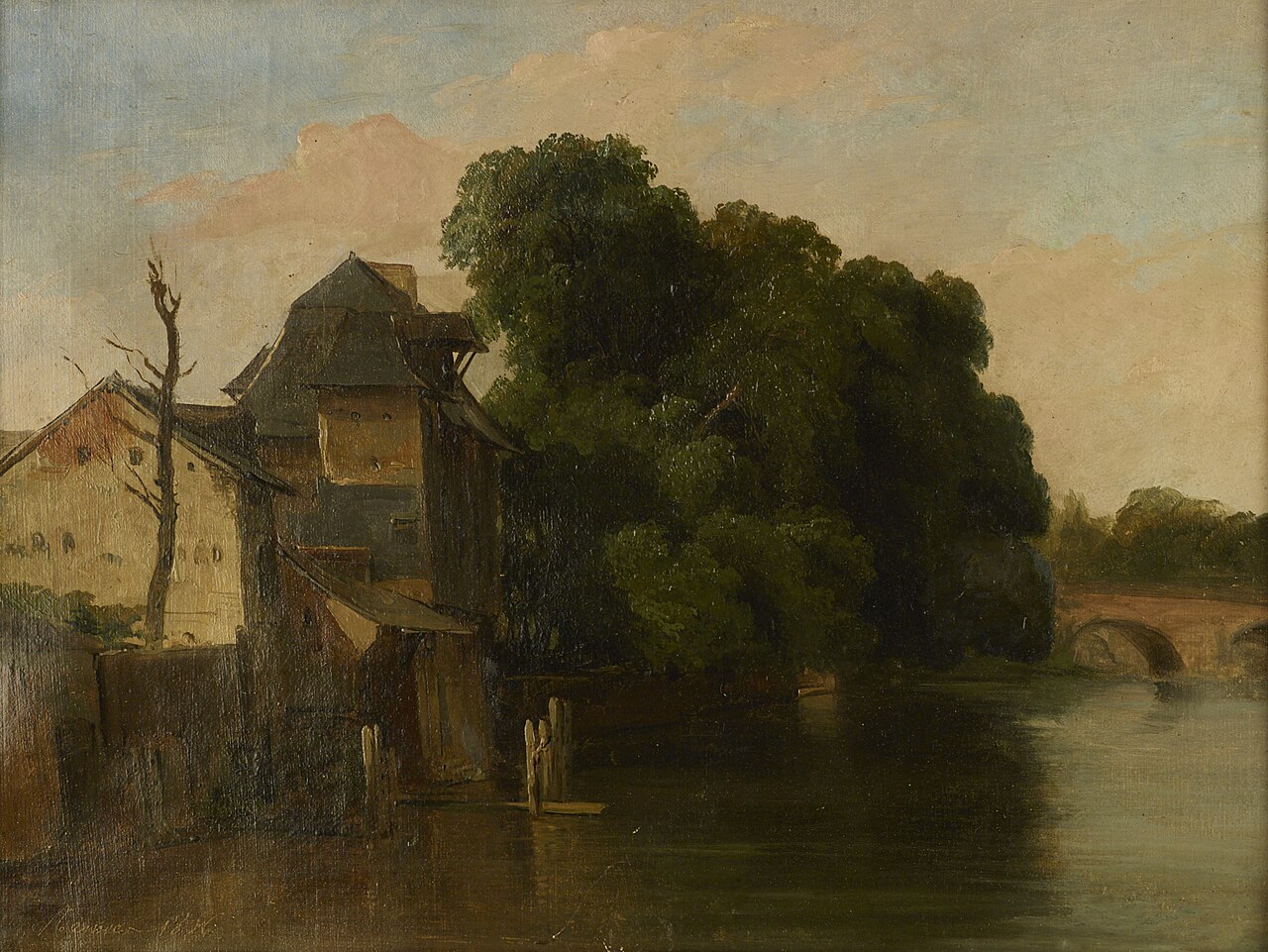 An old timber-roofed water mill and a large dark-green tree stand on the bank of the still Vilaine river in Rennes, with a stone arched bridge in the distance on the right under a warm evening sky.